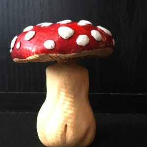May include: A decorative mushroom figurine with a red cap and white spots. The stem is a light beige color. The mushroom is displayed on a black surface.