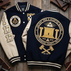 Op de afbeelding: Een marineblauwe en crèmekleurige varsity-jas met geborduurde vrijmetselaarsymbolen. De jas heeft de tekst "THE CRAFT FREEMASON" en "ANCIENT FREE & ACCEPTED MASONS". De mouwen hebben het nummer "1717". De jas heeft een gestreepte kraag en manchetten.