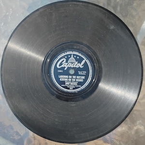 Puede incluir: Un disco de vinilo negro vintage con una etiqueta azul y blanca de Capitol Records. La etiqueta presenta "LAUGHING ON THE OUTSIDE (CRYING ON THE INSIDE)" de Andy Russell. Un objeto de colección de música clásica.
