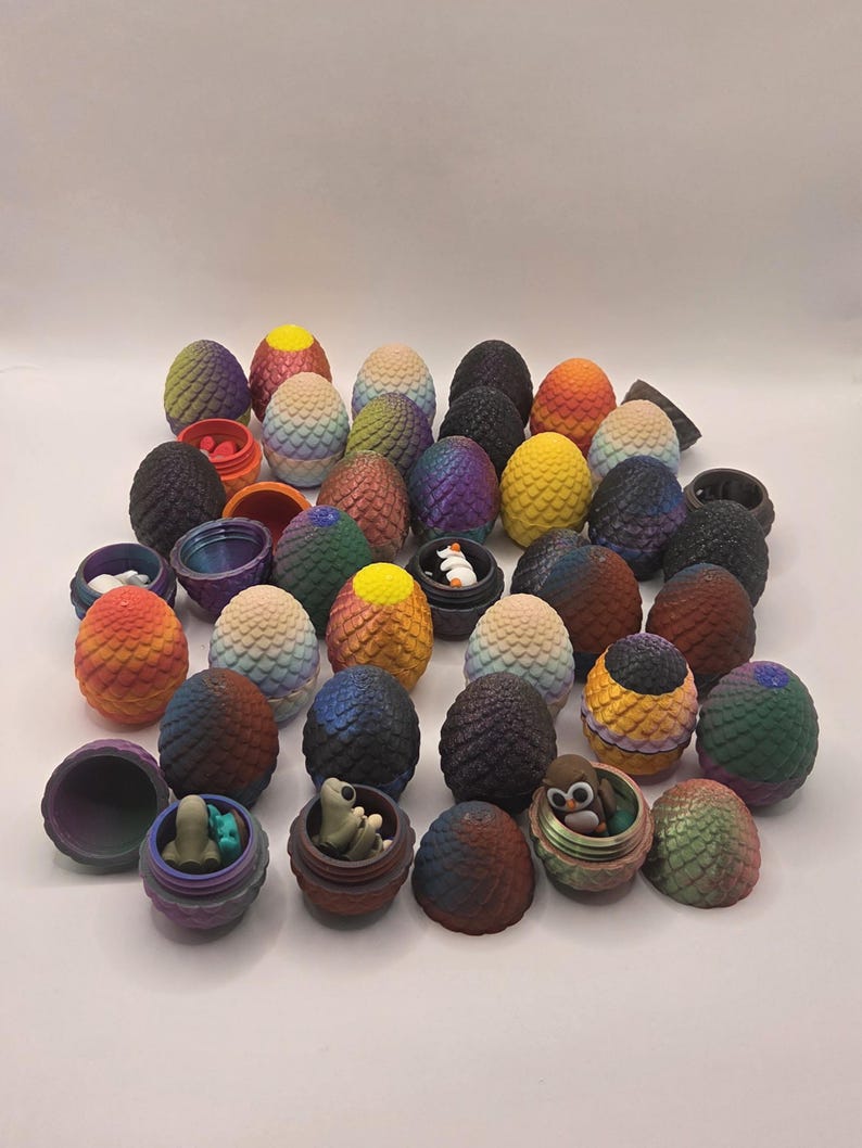 May include: A collection of decorative, colorful dragon egg-shaped containers. Some eggs are open, revealing small figurines inside. The eggs feature a variety of colors, including blue, green, orange, and purple. The containers are designed with a textured, scaled pattern.