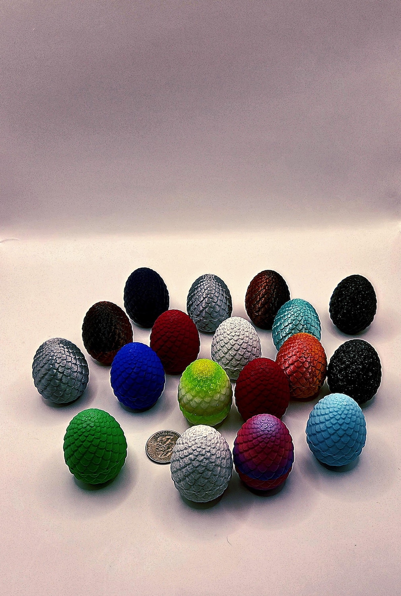 May include: A collection of decorative dragon eggs in various colors, including silver, blue, red, and green. Each egg has a textured, scaled surface. A US quarter is included for size reference.