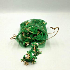 May include: A green sheer drawstring pouch filled with multiple small articulated frog figures. Each frog is green with beige skeletal details and white eyes. Two of these small frog figures are positioned outside the bag on the surface.
