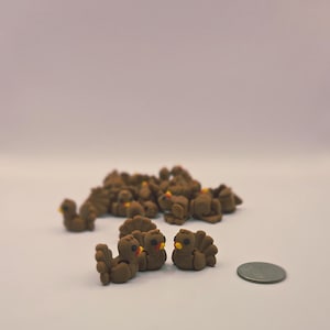 May include: A group of small, brown turkey figurines with yellow beaks and red snoods. The turkeys are clustered together, with a few in the foreground and many more in the background. A coin is next to the turkeys.