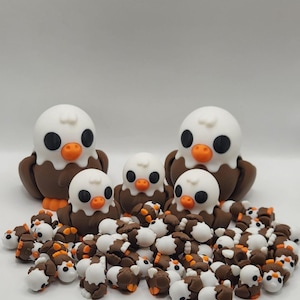 May include: A group of brown and white ceramic eagle figurines. There are three larger eagles and many smaller ones. The larger eagles have orange beaks and black eyes. The smaller eagles have brown beaks and black eyes.
