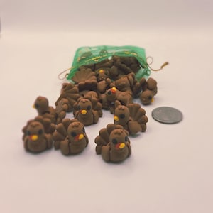May include: A group of small, brown turkey figurines with yellow beaks and red wattles. Some turkeys are spilling out of a green mesh bag. A coin is next to the turkeys. The figurines are likely for a craft project or holiday decoration.