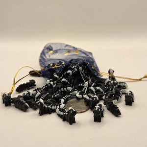 May include: A collection of small, black and white skunk-shaped beads spilling from a blue drawstring bag with gold accents. The beads are scattered on a white surface, with a US quarter coin visible.