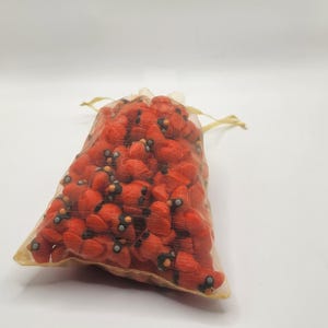 Pu&ograve; includere: Un piccolo sacchetto di rete dorata trasparente pieno di perline rosse e nere a forma di fiore.