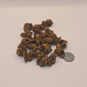 May include: A group of small, brown turkey-shaped polymer clay charms with yellow and red details. The charms are scattered on a white surface, with a coin for scale. These miniature figurines are likely for crafting or jewellery making.