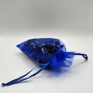 K&ouml;nnte beinhalten: Eine blaue Kordeltasche aus durchsichtigem Stoff mit einem wei&szlig;en und schwarzen Muster. Die Tasche ist mit kleinen, runden Gegenst&auml;nden gef&uuml;llt.