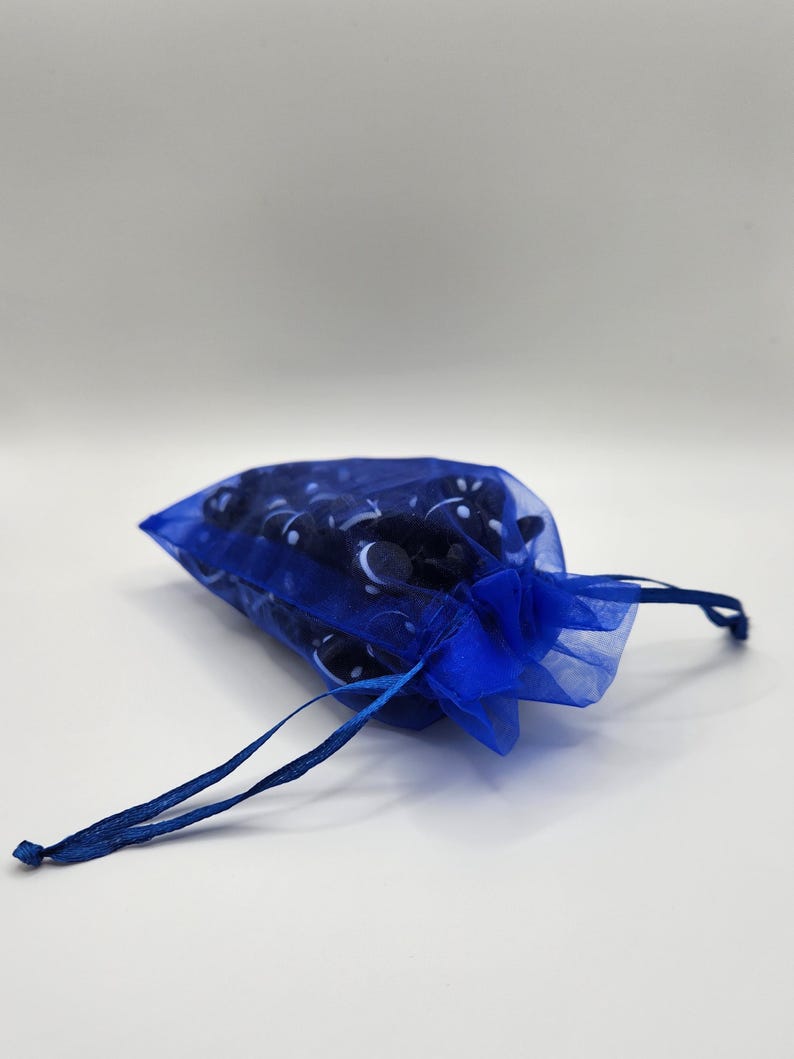 K&ouml;nnte beinhalten: Eine blaue Kordeltasche aus durchsichtigem Stoff mit einem wei&szlig;en und schwarzen Muster. Die Tasche ist mit kleinen, runden Gegenst&auml;nden gef&uuml;llt.