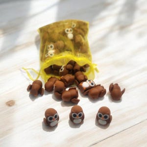 May include: A yellow mesh bag filled with small brown owl figurines. Several owls are scattered on a white wooden surface.