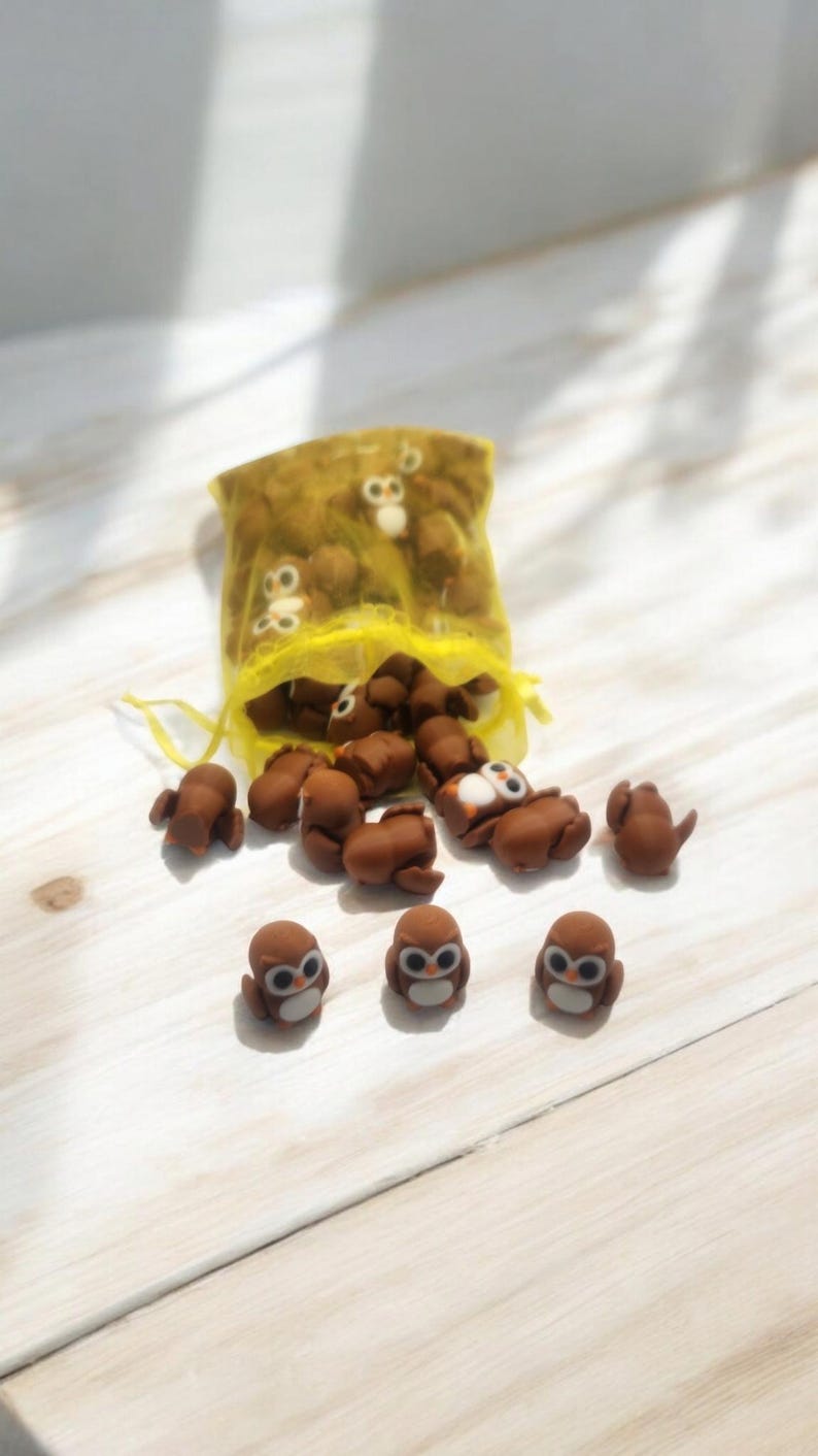 May include: A yellow mesh bag filled with small brown owl figurines. Several owls are scattered on a white wooden surface.