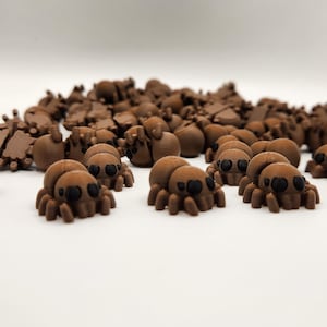 May include: A group of small, brown, 3D printed spiders with black eyes. The spiders are scattered on a white surface.