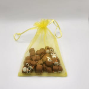 May include: A yellow organza bag filled with small brown owl-shaped erasers.