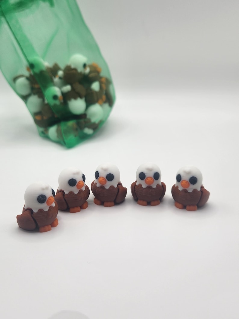 May include: Five small brown and white eagle figurines with black eyes and orange beaks. The figurines are arranged in a line on a white surface.