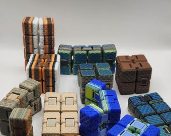 May include: A collection of colorful fidget cubes in various designs. The cubes feature a variety of colors, including blue, green, orange, brown, and beige. The cubes are made of plastic and have a textured surface.