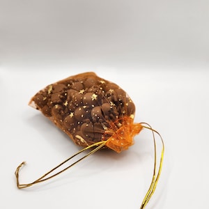 May include: A small orange mesh bag with gold stars printed on it. The bag is filled with small, round, brown chocolate sweets and tied with a gold ribbon.