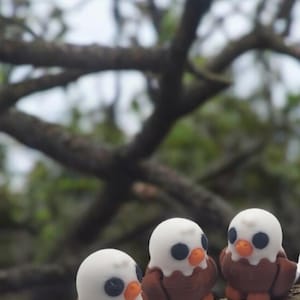 May include: Three small, brown and white bird figurines perched on a tree branch. The birds have black eyes and orange beaks.