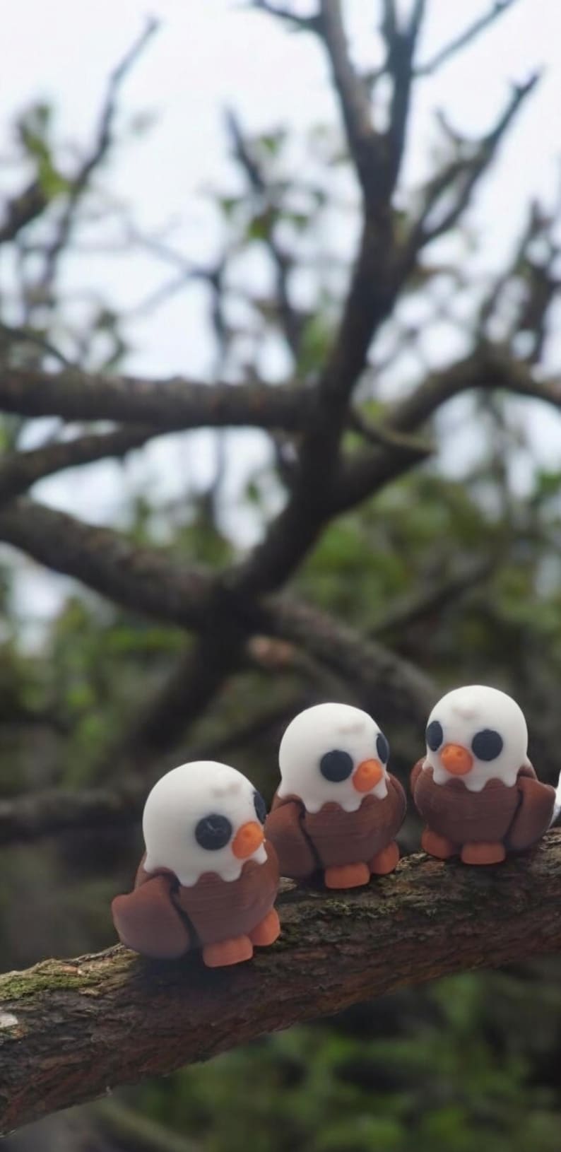 May include: Three small, brown and white bird figurines perched on a tree branch. The birds have black eyes and orange beaks.