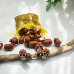 May include: A yellow mesh bag filled with small brown owl figurines. Some of the owls are sitting on a brown branch.
