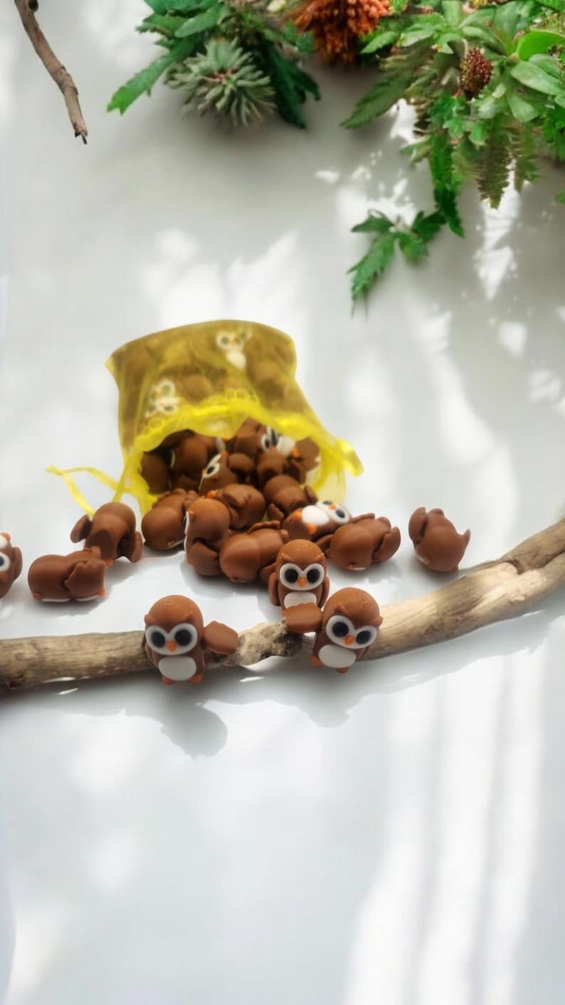 May include: A yellow mesh bag filled with small brown owl figurines. Some of the owls are sitting on a brown branch.