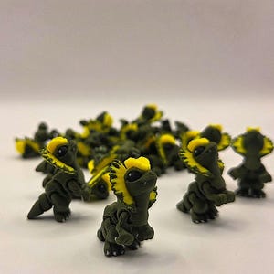 May include: A collection of small, dark green dinosaur figurines with bright yellow frills around their heads. The figurines are clustered together, with several in sharp focus, showcasing their detailed features and playful design.