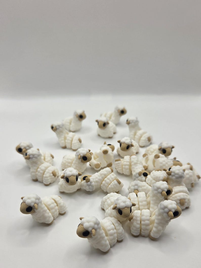 May include: A collection of small, white sheep figurines with tan faces and hooves. The sheep are arranged in a group, with some lying down and others standing. The figurines have a textured, wool-like appearance.