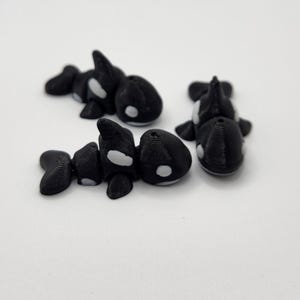 K&ouml;nnte beinhalten: Drei kleine, schwarz-wei&szlig;e 3D-gedruckte Orca-Figuren. Die Orcas haben wei&szlig;e Flecken auf R&uuml;cken und Bauch.