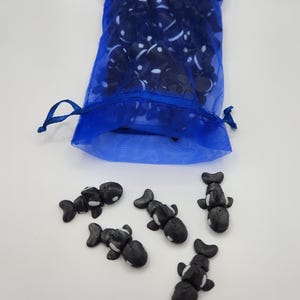 K&ouml;nnte beinhalten: Ein blauer Netzbeutel gef&uuml;llt mit schwarzen und wei&szlig;en Orca-Figuren. F&uuml;nf Orca-Figuren liegen verstreut auf einer wei&szlig;en Oberfl&auml;che.