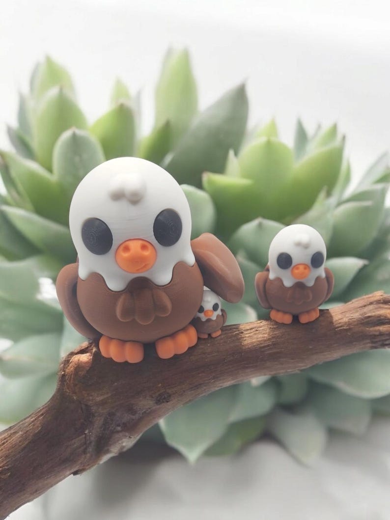 May include: Three brown and white bird figurines with large eyes, perched on a branch. The largest bird has a white head and beak, while the smaller birds have white heads and black beaks.