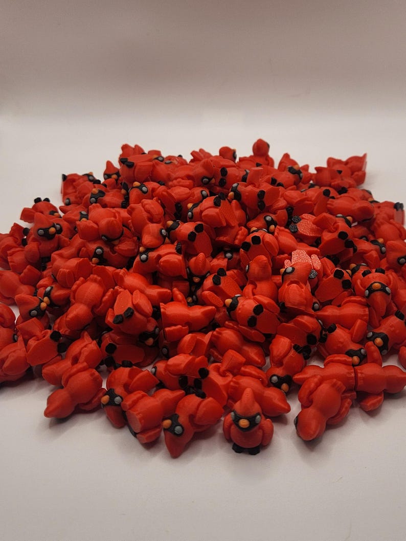 Pu&ograve; includere: Un grande mucchio di piccole figurine di cardinali rossi. Le figurine sono fatte di un materiale rosso liscio e hanno occhi e becchi neri.