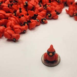 Pu&ograve; includere: Un mucchio di piccole figurine di cardinali rossi con occhi e becchi neri, con una figurina di cardinale seduta su una moneta da un quarto di dollaro americano.