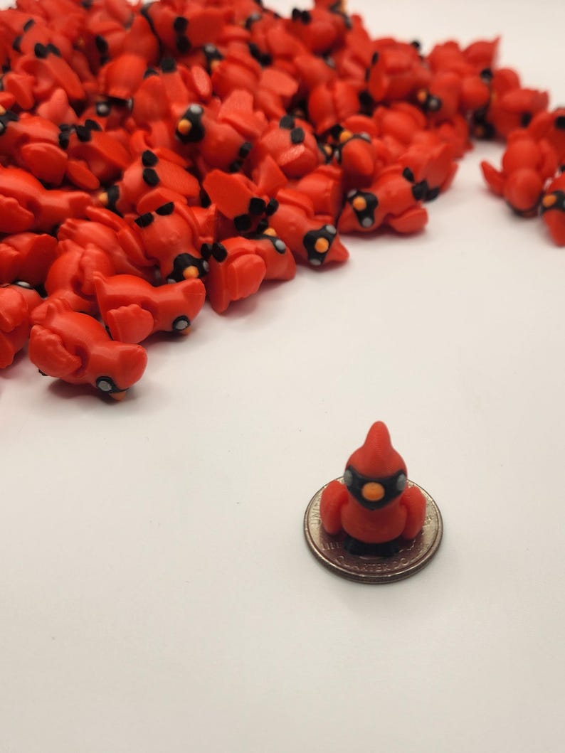 Pu&ograve; includere: Un mucchio di piccole figurine di cardinali rossi con occhi e becchi neri, con una figurina di cardinale seduta su una moneta da un quarto di dollaro americano.