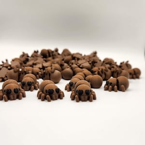 May include: A large group of brown plastic spiders with black eyes. The spiders are scattered on a white surface.