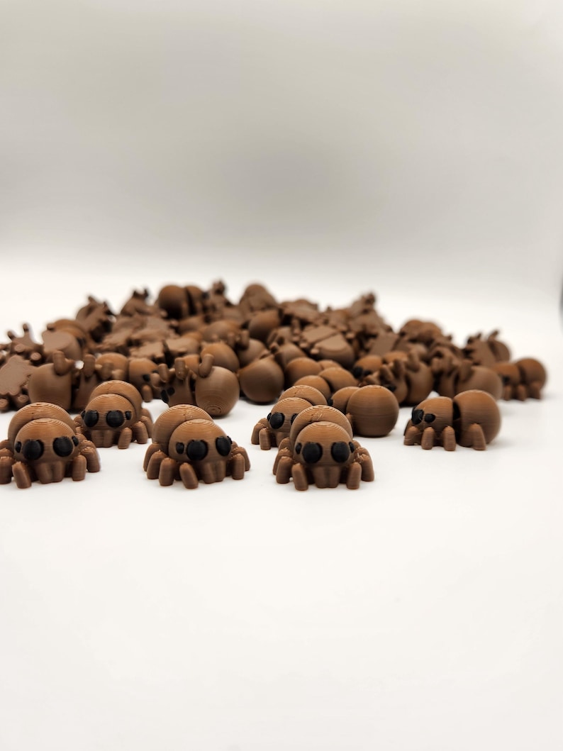 May include: A large group of brown plastic spiders with black eyes. The spiders are scattered on a white surface.