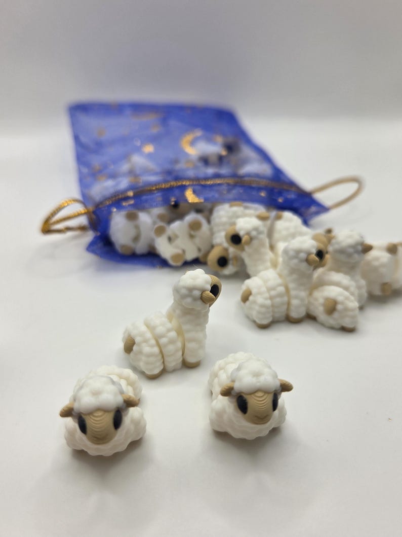 May include: A collection of small, white sheep figurines with tan faces and ears. Some sheep are upright, others are lying down. They are spilling out of a blue mesh bag with gold accents.