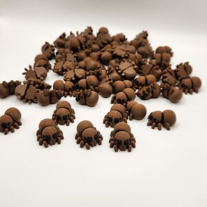 May include: A large group of brown plastic spiders with black eyes. The spiders are scattered on a white surface.