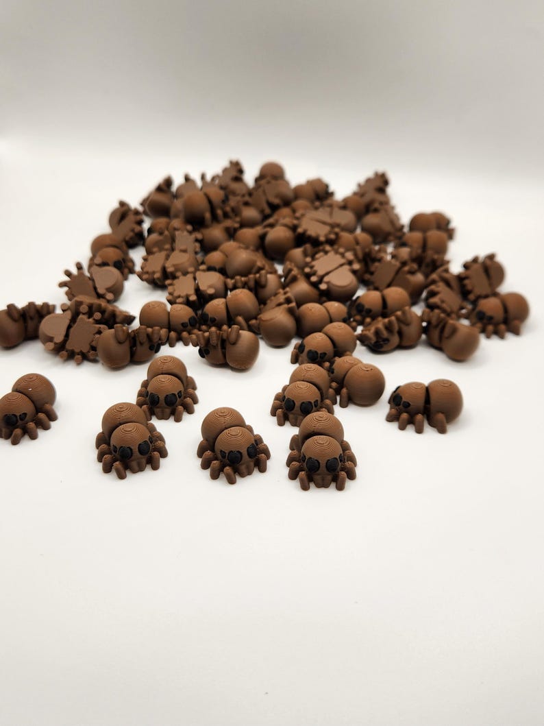 May include: A large group of brown plastic spiders with black eyes. The spiders are scattered on a white surface.