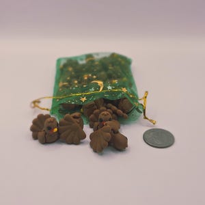 May include: Small, brown turkey figurines with orange beaks and red wattles, scattered near a green mesh bag with gold detailing. A UK coin is next to the turkeys.