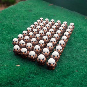 May include: A group of small, brown and white ceramic figurines of bald eagles arranged in a triangular formation on a green surface.