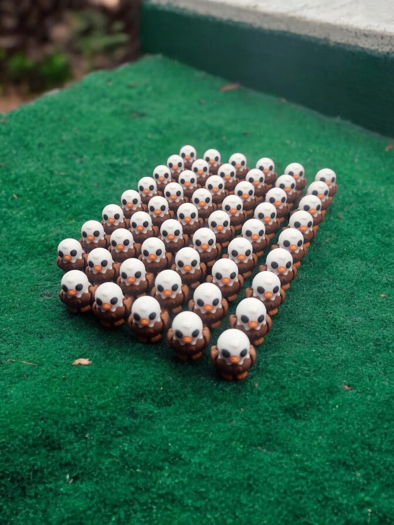 May include: A group of small, brown and white ceramic figurines of bald eagles arranged in a triangular formation on a green surface.