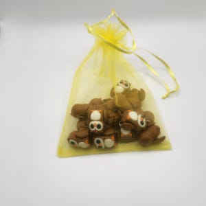 May include: A yellow organza bag filled with brown owl-shaped erasers. The owls have white eyes and black pupils.