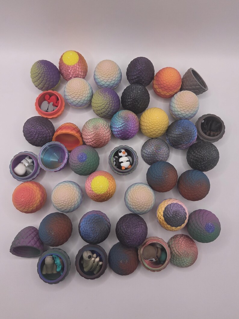 May include: A collection of colorful, spherical toys, some opened to reveal small figurines. The spheres have textured surfaces and are in shades of purple, blue, yellow, and orange. Some toys are open, displaying miniature figures inside.