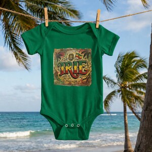 Może przedstawiać: Zielone body dla dziecka z kolorową grafiką z napisem "IRIE" dużymi literami. Grafika zawiera również frazy "Living an IRIE Life" i "Peace & Love". Body wisi na sznurku do wieszania prania, w tle plaża i palmy.