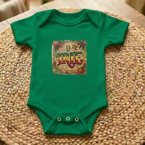 Puede incluir: Body de bebé verde con un gráfico colorido que dice "IRIE". El gráfico también incluye las frases "Living an True Life" y "Peace & Love". El body tiene tres broches en la parte inferior.