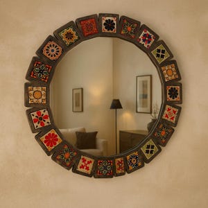 May include: Round decorative mirror with a dark wooden frame. The frame is adorned with square, colorful tiles featuring floral and geometric patterns in red, yellow, blue, and green. The mirror reflects a room with furniture and a lamp.