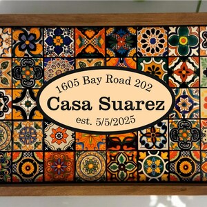 May include: A wooden serving tray with a vibrant tile pattern. The tray has an oval label with the text "1605 Bay Road 202 Casa Suarez est. 5/5/2025". The tiles are in shades of blue, orange, yellow, and green.