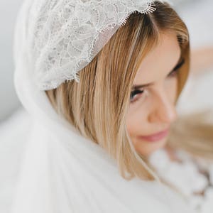 May include: A white bridal veil with a delicate lace trim. The veil is draped over the bride's head and shoulders.