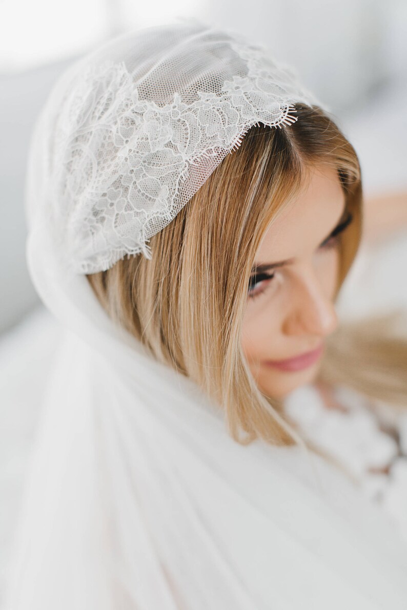 May include: A white bridal veil with a delicate lace trim. The veil is draped over the bride's head and shoulders.
