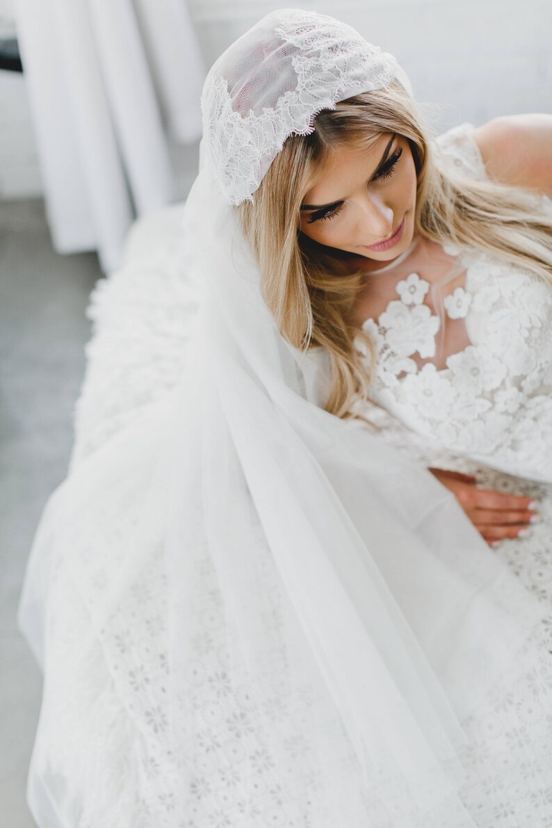 May include: A bride wearing a white lace wedding dress with a white veil and a lace headpiece.